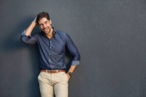 Portrait of smart business man standing and laughing against gray wall. Confident entrepreneur feeling excited on success and looking at camera. Young businessman in casual clothing smiling isolated on grey background with copy space.