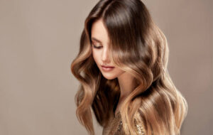 Young, beautiful brown haired woman is demonstrating wavy, dense, dyed long hair. Shades of brown color in a locks of hair. Multilayer, complex colouring of woman hair. Modern trends of hair dye. Hairdressing art and hair care.
