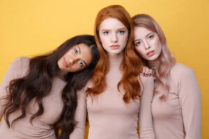 Two women lying on shouldres their friend over yellow backgrounf