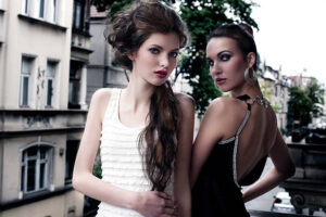 fashion shot of two attractive and elegant girl friend outside in a balcony with old fashion style building in background